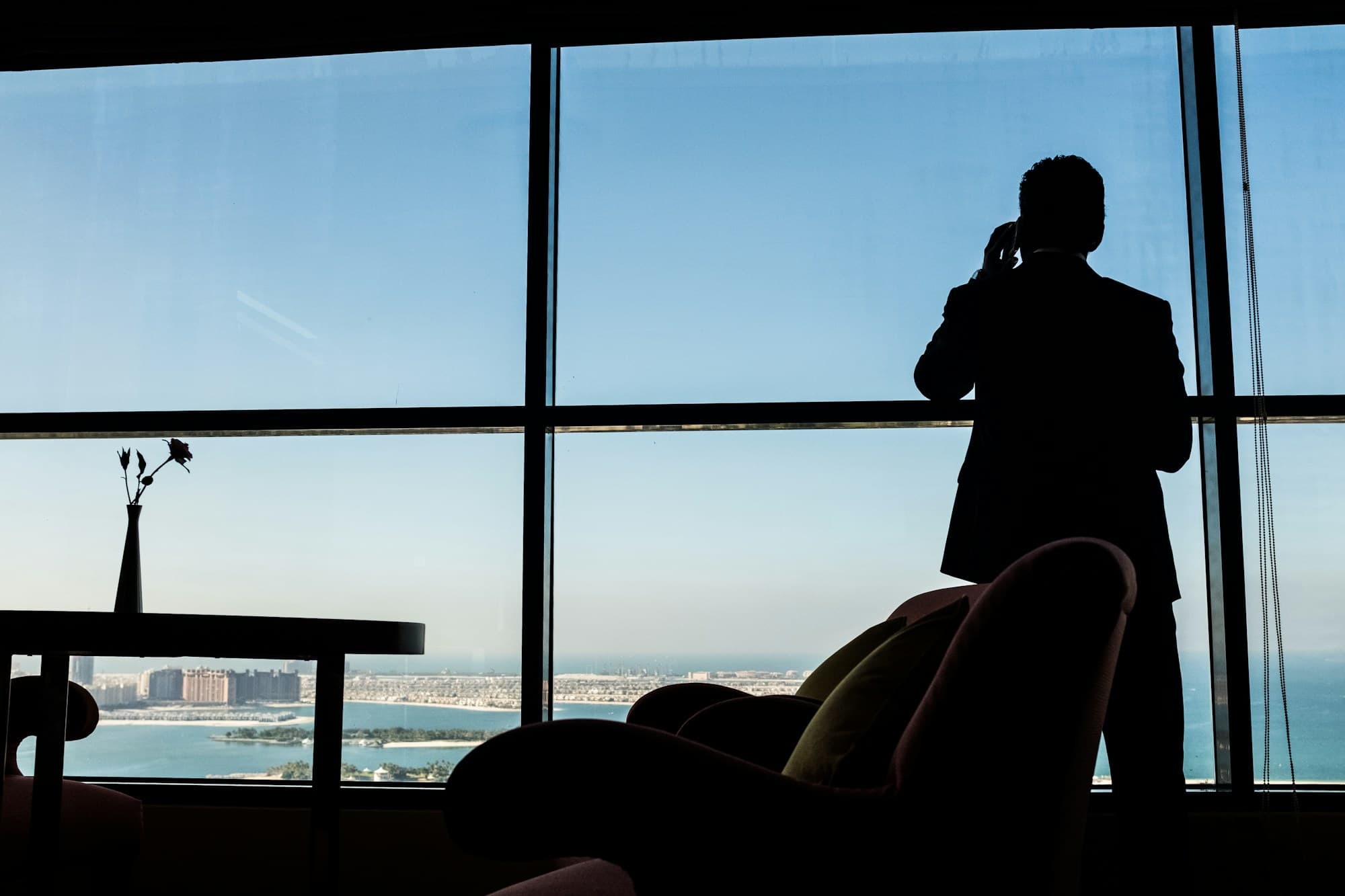Silhouette of an executive in a suit taking a phone call at a floor-to-ceiling window high above the city
